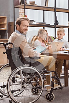 father on wheelchair teaching children at home and looking