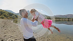 Father whirls his daughter near the lake in slow