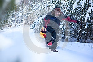 Father in winter clothes pulling sledges with his son in winter snowy forest. Happy family walk in snowy forest