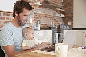 Father Working From Home On Laptop With Baby Son