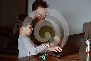 A father is working on a laptop while his little son is standing next to him and pointing at the monitor. photo