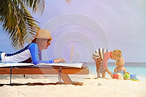 Father working on laptop while kids play at beach