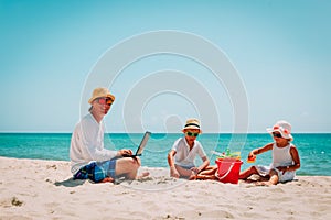 Father working on laptop while kids play at beach