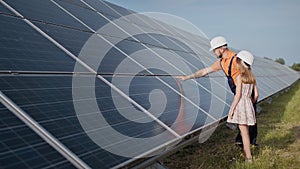 A father working in a solar power plant tells his daughter about his work, shows green energy, solar panels. Shooting at