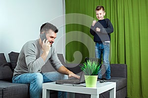 Father works on a laptop at home, his son bothers him. Businessman working from home and looking after a child, spending time with
