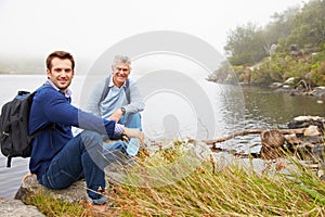 Father and young adult son sitting by a lake