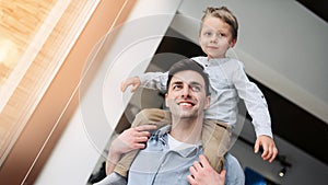 A father with a young son are fooling around while sitting on the sofa. The boy sits on his father's shoulders.