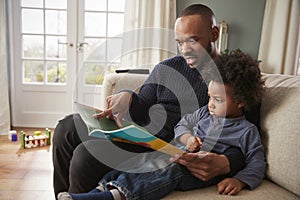 Father And Young Son Reading Book Together At Home