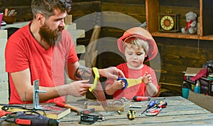 Fatherhood concept. Boy, child busy in protective helmet learning to use handsaw with dad. Father, parent with beard