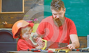 Fatherhood concept. Boy, child busy in protective helmet learning to use handsaw with dad. Father, parent with beard