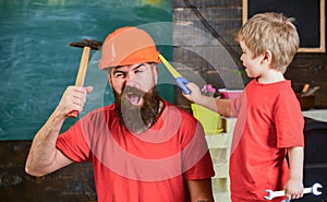 Fatherhood concept. Father, parent with beard in protective helmet teaching little son to use different tools in school