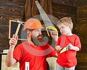 Fatherhood concept. Father, parent with beard in protective helmet teaching son to use different tools in school