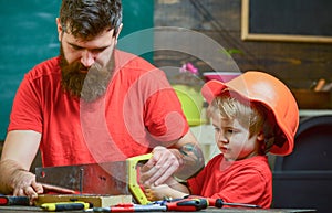 Fatherhood concept. Father, parent with beard teaching little son to sawing with sharp handsaw, carpenter crafts. Boy