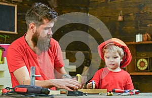 Fatherhood concept. Father, parent with beard teaching little son to sawing while son play with toy saw. Boy, child busy