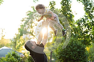 Fatherhood, parenthood, childhood, caring, summer and leisure concept - young dad with beard and long hair in black t