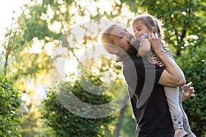 Fatherhood, parenthood, childhood, caring, summer and leisure concept - young dad with beard and long hair in black t