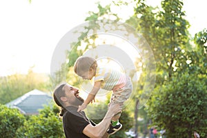 Fatherhood, parenthood, childhood, caring, summer and leisure concept - young dad with beard and long hair in black t