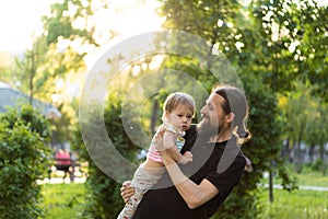 Fatherhood, parenthood, childhood, caring, summer and leisure concept - young dad with beard and long hair in black t