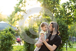 Fatherhood, parenthood, childhood, caring, summer and leisure concept - young dad with beard and long hair in black t