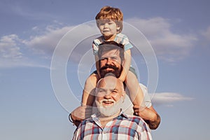 Fathers day - grandfather, father and son are hugging and having fun together. Happy child playing against summer sky