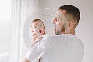 Fathers Day. Happy Caucasian father holding newborn baby. Man parent imitating his yawning child daughter son. Authentic lifestyle