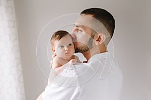 Fathers Day holiday. Bearded Caucasian father kissing newborn baby girl. Parent holding rocking child daughter son on hands.