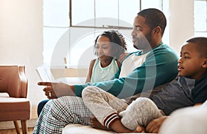 Fathers are their sons first hero and daughters first love. a father and his children reading a book indoors.