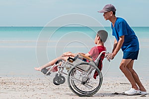 Fatherâ€‹ and Asian special child on wheelchair playing, doing activity on  sea beach in summer,