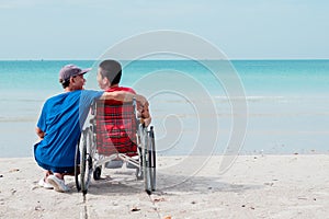 Fatherâ€‹ and Asian special child on wheelchair playing, doing activity on  sea beach in summer,