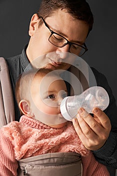 Fathre and his kid in baby carrier at the grey background wall, baby wearing concept