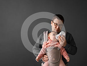 Fathre and his kid in baby carrier at the grey background wall, baby wearing concept