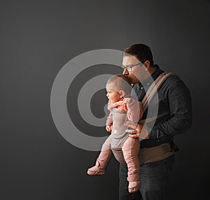 Fathre and his kid in baby carrier at the grey background wall, baby wearing concept