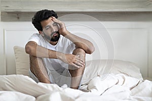 Fatigue Concept. Tired Young Indian Man Sitting In Bed At Home