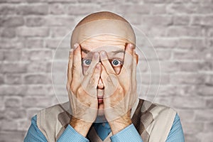 Fatigue, Crisis Concept - Portrait bald Man Peers Through His Fingers on brick wall white background