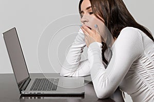 Fatigue at work and sleep deprivation. exhausted woman yawning, sitting at table and working at laptop