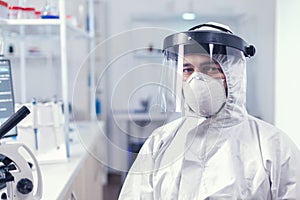 Fatigued medical scientist sitting at workplace wearing coverall against covid19 photo