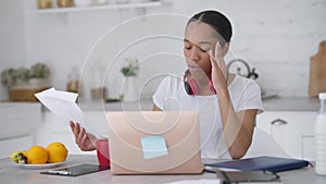 Fatigued overwhelmed young African American woman sighing throwing away paperwork holding head in hands. Portrait of