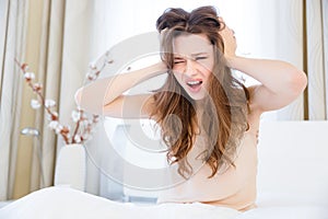 Fatigued woman sitting on bed with eard closed by hands