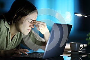 Fatigued woman suffering eyestrain using laptop at night