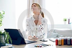 Fatigued young woman with neck pain working with her digital tablet at the office