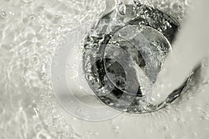 Faucet running on bathroom chrome drain stopper with water and bubbles