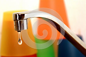 Faucet and waste of water with colorful glasses on background