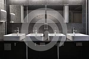 Faucets with washbasin in public restroom in grey colors