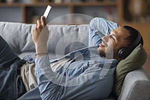 Favorite Leisure. Happy Black Guy In Wireless Headphones Listening Music On Smartphone