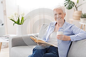 Favorite Pastime. Senior woman relaxing with book and hot tea at home