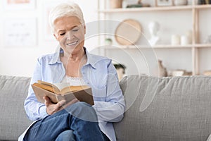 Favorite Pastime. Smiling Elderly Lady Reading Book On Comfortable Couch At Home