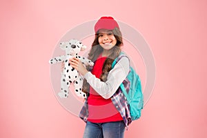 Favorite toy. Happy small child hold soft toy on pink background. Little girl in hipster style smile with toy dog. Kids