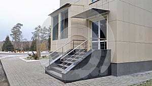 The faÃ§ade of the building and the surrounding area are lined with different types of tiles. A porch with metal handrails leads t