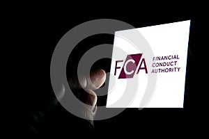 FCA Financial Conduct Authority logo on the smartphone and finger pointing at it in the dark room. Concept.