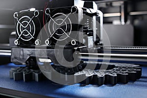 FDM 3D-printer manufacturing spur gears from silver-gray filament on blue print tape in bright light